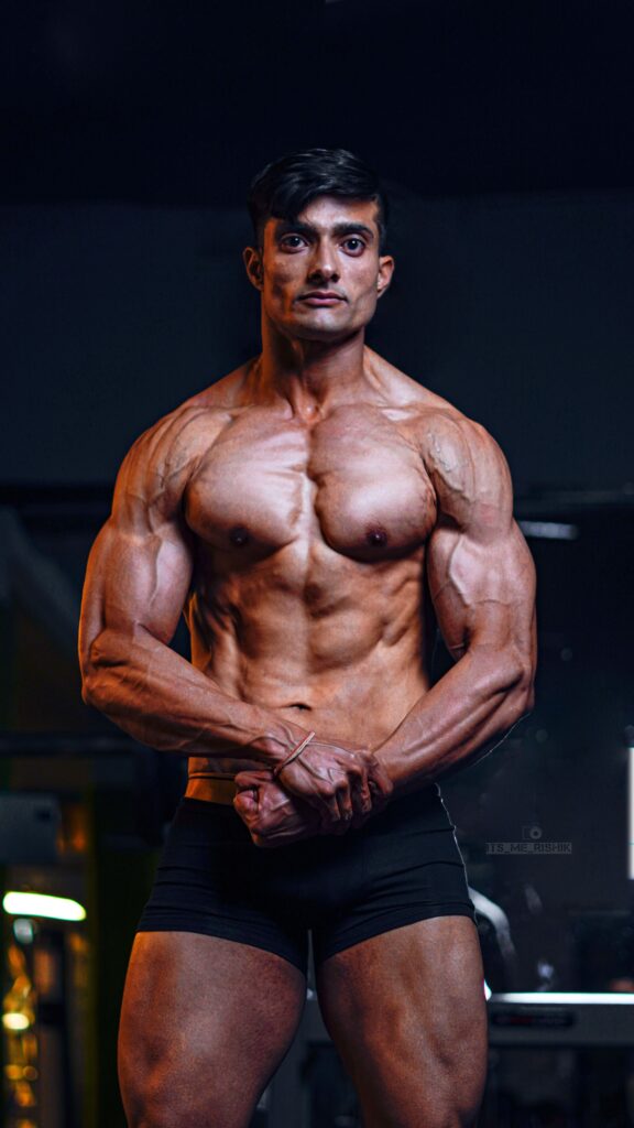 A brawny South Asian bodybuilder flexing muscles in a gym, showcasing strength and masculinity.