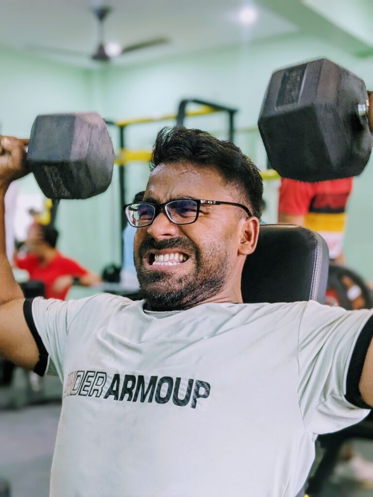 Focused man lifting heavy dumbbells in a gym setting, showing determination and strength.