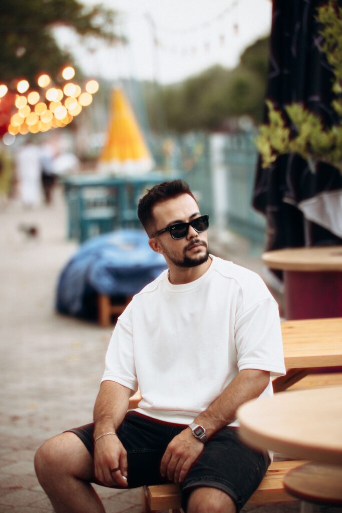 Stylish man in sunglasses and white t-shirt sitting at an outdoor café.
